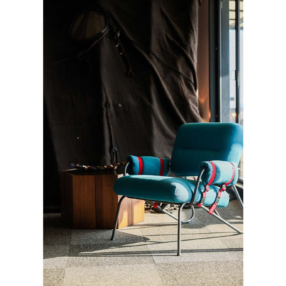 Teal upholstered armchair with chrome legs and red accent straps.